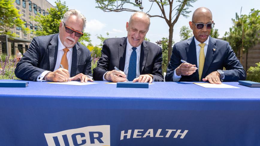 image of three men signing documents sitting on a table that reads UCR Health