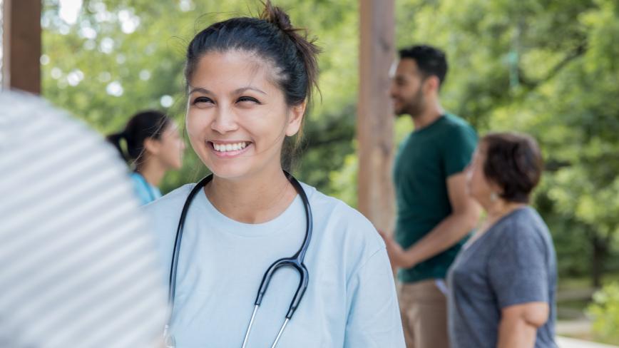 Image of a health care professional outside smiling with people in the background