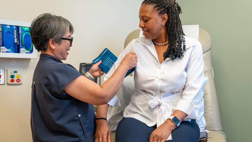 UC health professional taking blood pressure measurement of a person sitting in an exam room