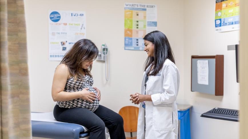 UC clinician standing next to a seated patient in a clinic exam room