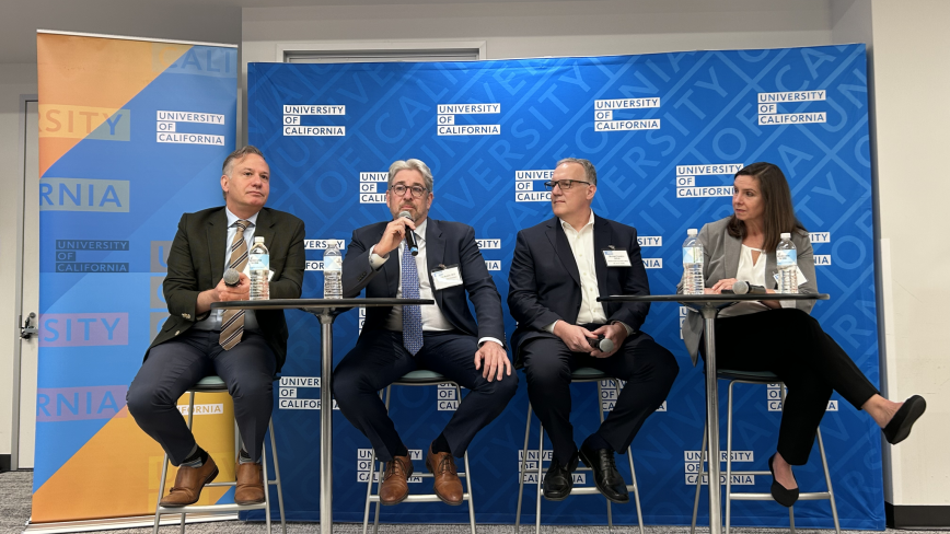 Image of four health system leaders at a panel in front a UC blue and gold step-and-repeat