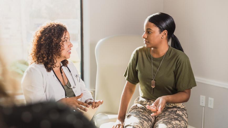health care professional in white coat speaking with veterans patient in military fatigues