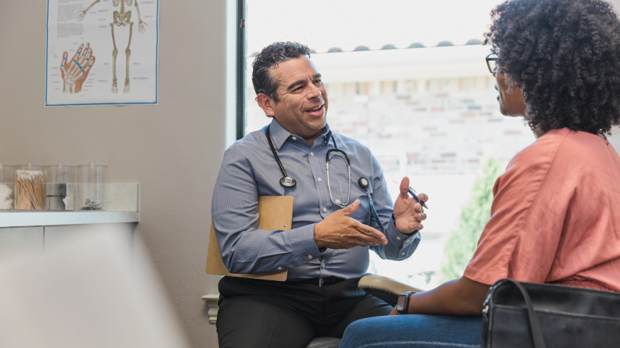 image of a health professional in a grey shirt smiling at a patient inside a doctor's office