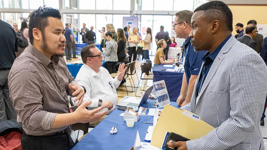 Two people talk across a table at a network event with brochures on a blue tablecloth