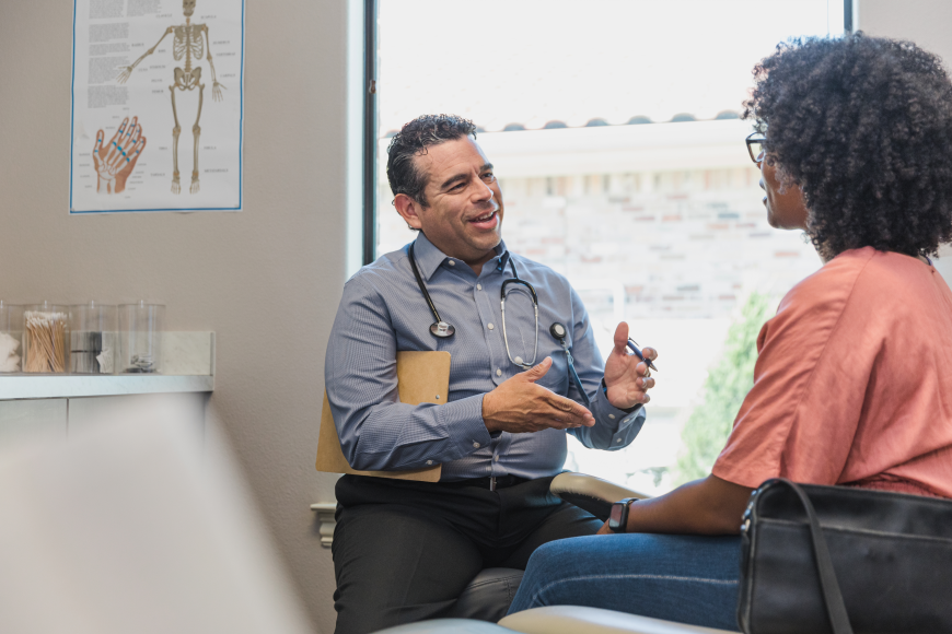 Doctor in a doctor's office speaking to a patient with a poster of a skeleton behind them