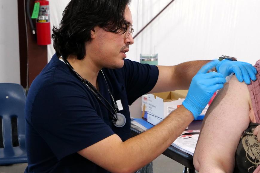 A health professional, as part of The Grow Grants awarded program, wears blue medical gloves as they provide a shot in a patient's arm